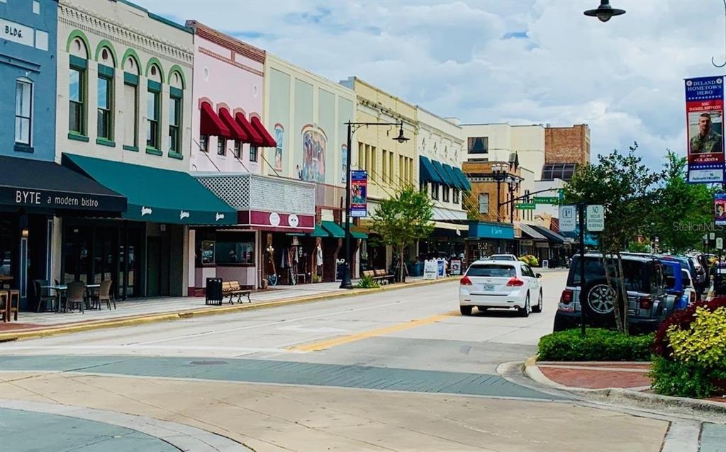 A street view of a downtown area with historic storefronts, parked cars, and a banner — 2505 OLD NEW YORK AVENUE, DELAND, FL