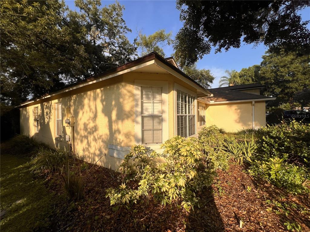 A yellow stucco house exterior features a corner window and surrounding landscaping under trees — 1320 SASSAFRAS AVENUE, ALTAMONTE SPRINGS, FL