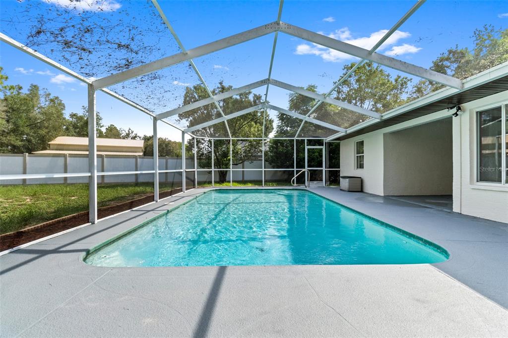 A rectangular swimming pool is enclosed by a screened lanai with a concrete deck — 132 GILLIAN DRIVE, SPRING HILL, FL