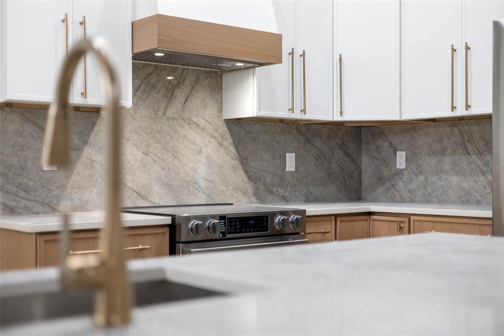 A kitchen features white upper cabinets, wood lower cabinets, stone countertops, and a stone backsplash — 132 GILLIAN DRIVE, SPRING HILL, FL