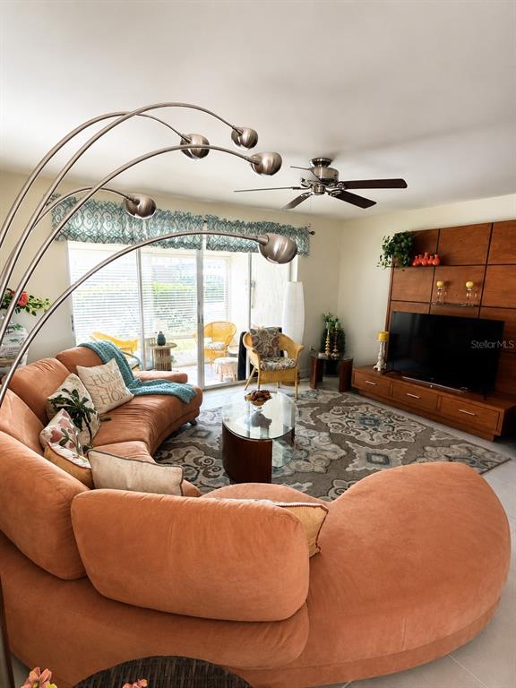 A living room features a large curved orange sofa, a television console, and a ceiling fan — 3720 EL POINIER COURT UNIT 515, SARASOTA, FL
