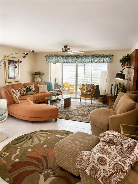 A living room features a large curved orange sofa, patterned area rugs, and sliding glass doors — 3720 EL POINIER COURT UNIT 515, SARASOTA, FL