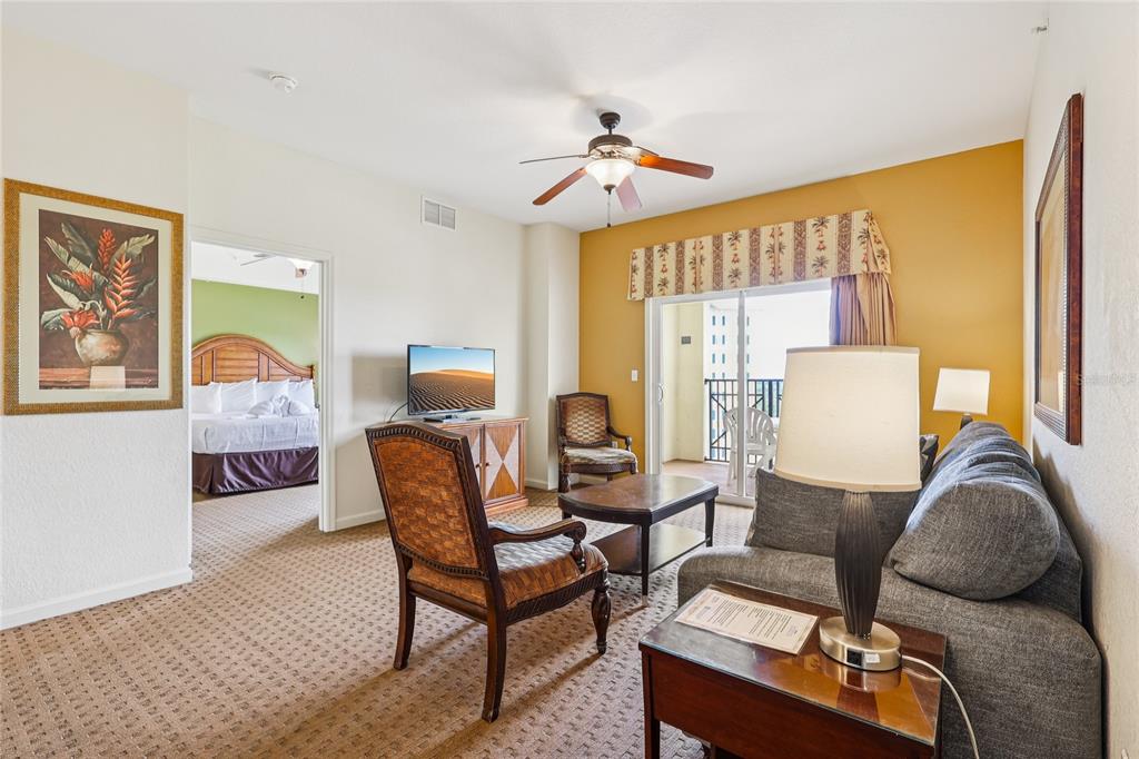 A living room with a gray sofa, patterned chair, and a doorway leading to a bedroom — 8101 RESORT VILLAGE DRIVE UNIT 31210, ORLANDO, FL