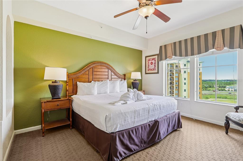 A bedroom features a king bed with a wooden headboard, green wall, and large windows — 8101 RESORT VILLAGE DRIVE UNIT 31210, ORLANDO, FL