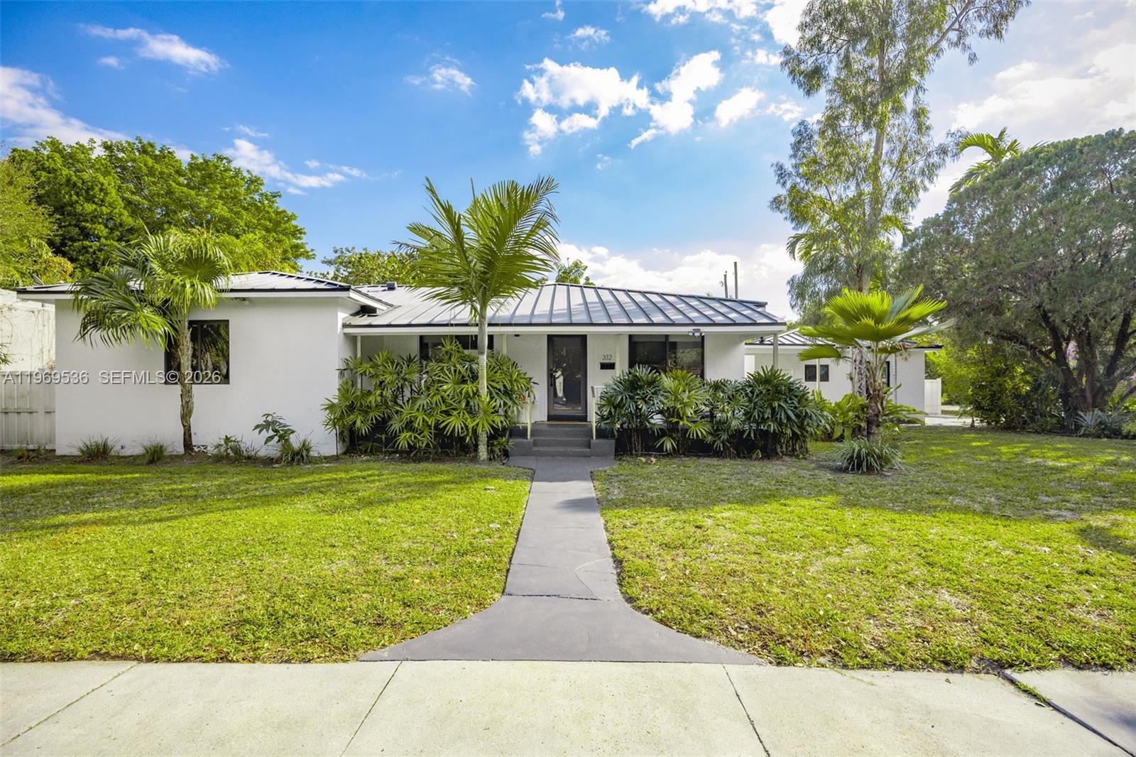 A single-story white house with a metal roof sits behind a concrete walkway and lawn — 312 NE 90th St, El Portal FL 33138, EL PORTAL, FL