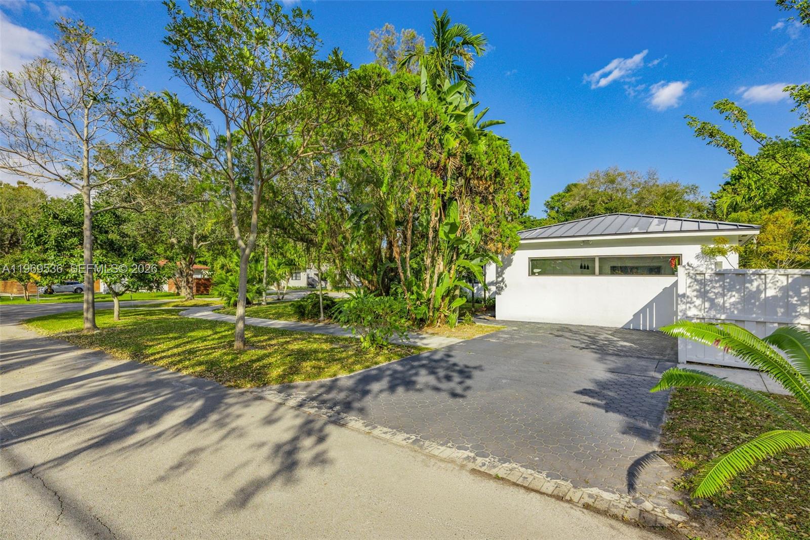 A white building with a metal roof sits beside a paved driveway and lush trees — 312 NE 90th St, El Portal FL 33138, EL PORTAL, FL