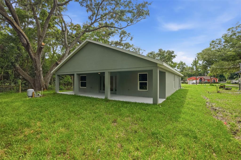 A rear view of a gray house with a covered patio and a large lawn — 352 GARFIELD AVENUE, MASARYKTOWN, FL
