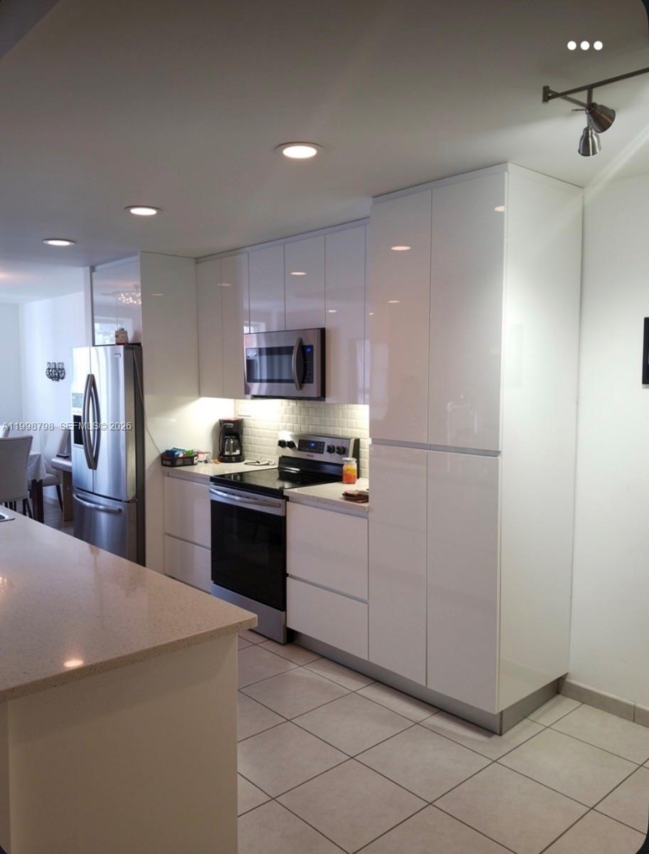 A modern kitchen features white high-gloss cabinets, stainless steel appliances, and light-colored tile flooring — 3301 Raleigh St # 4A, Hollywood FL 33021, HOLLYWOOD, FL