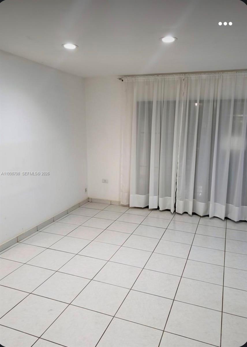 An empty room features white walls, light-colored tiled flooring, and floor-to-ceiling white curtains — 3301 Raleigh St # 4A, Hollywood FL 33021, HOLLYWOOD, FL