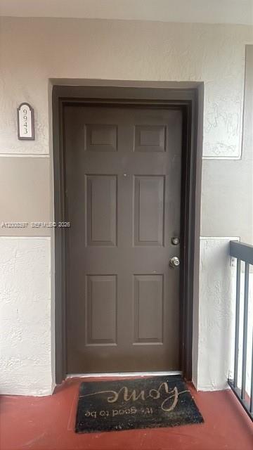 A brown six-panel front door with a welcome mat on a red porch — 9943 Nob Hill Pl # 9943, Sunrise FL 33351, SUNRISE, FL