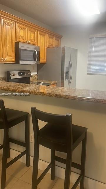 A kitchen features wood cabinets, stainless steel appliances, a granite countertop, and two bar stools — 9943 Nob Hill Pl # 9943, Sunrise FL 33351, SUNRISE, FL