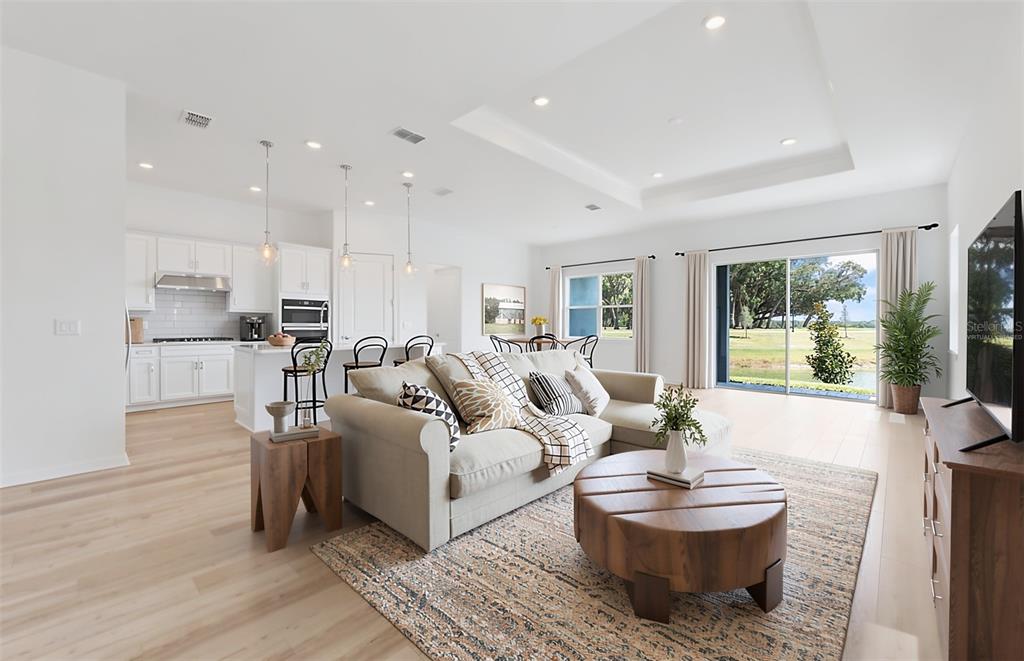 A bright open-concept living room and kitchen featuring light wood floors and a sliding glass door — 34754 LOWERY TRAIL, ZEPHYRHILLS, FL