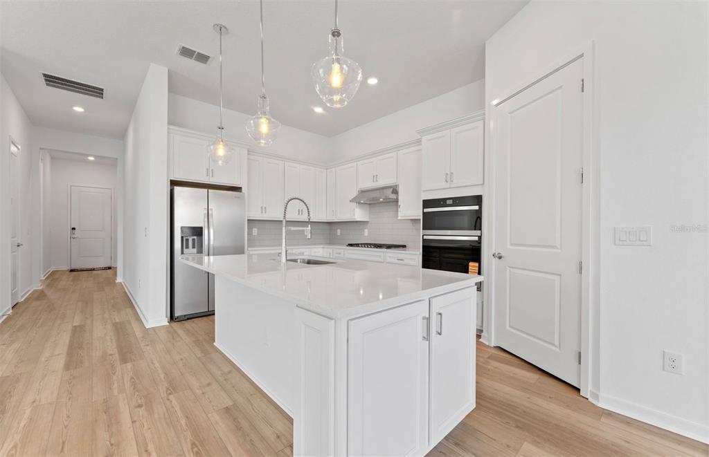 A modern kitchen features white cabinetry, a large center island, and stainless steel appliances — 34754 LOWERY TRAIL, ZEPHYRHILLS, FL