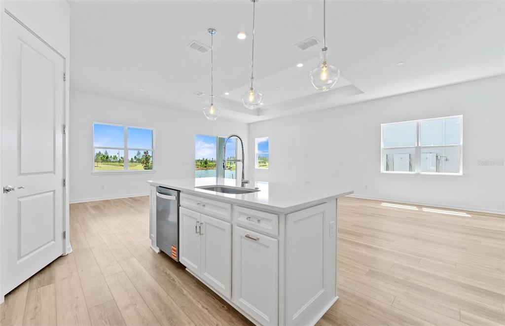 A bright kitchen features a white island with a sink, pendant lighting, and wood flooring — 34754 LOWERY TRAIL, ZEPHYRHILLS, FL