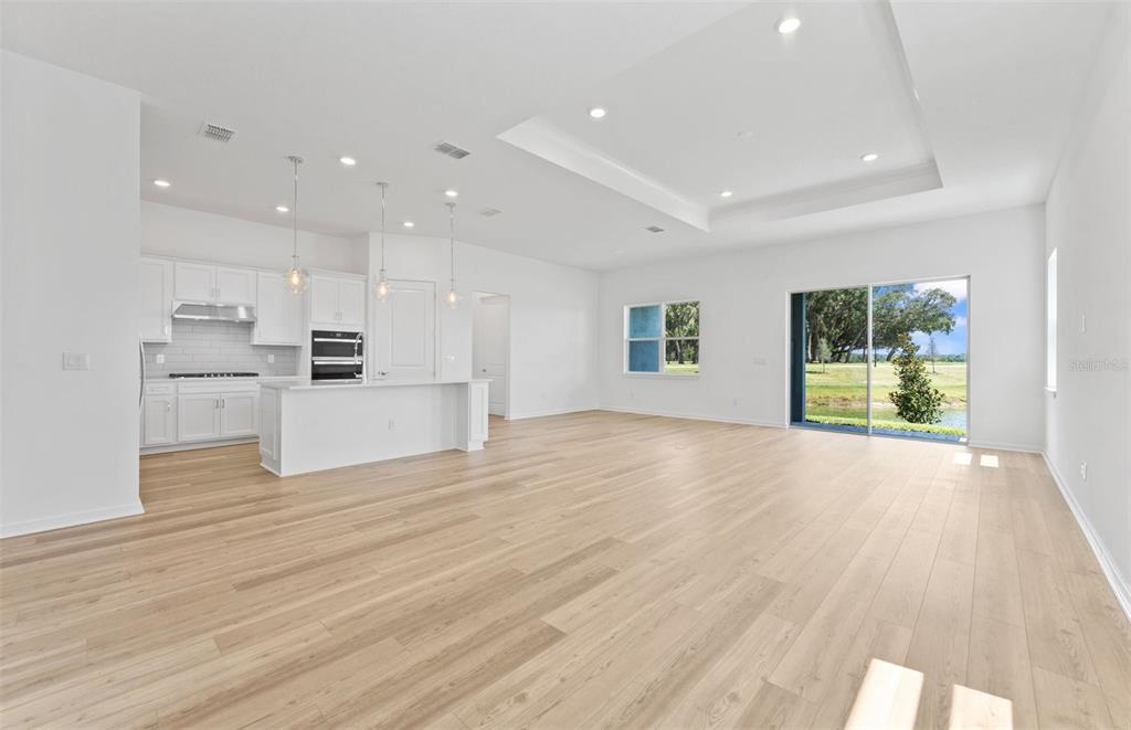 A bright, open-concept kitchen and living area features white cabinetry, light wood flooring, and sliding doors — 34754 LOWERY TRAIL, ZEPHYRHILLS, FL
