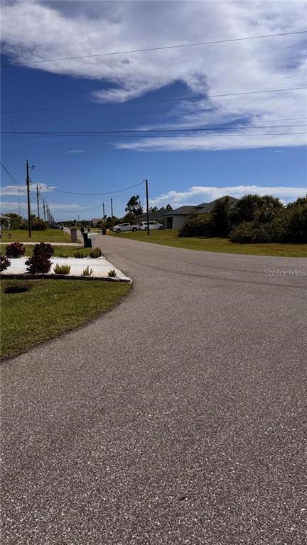 A paved residential street curves past a grassy lot with small shrubs and utility poles — 320 BAYTREE DRIVE, ROTONDA WEST, FL