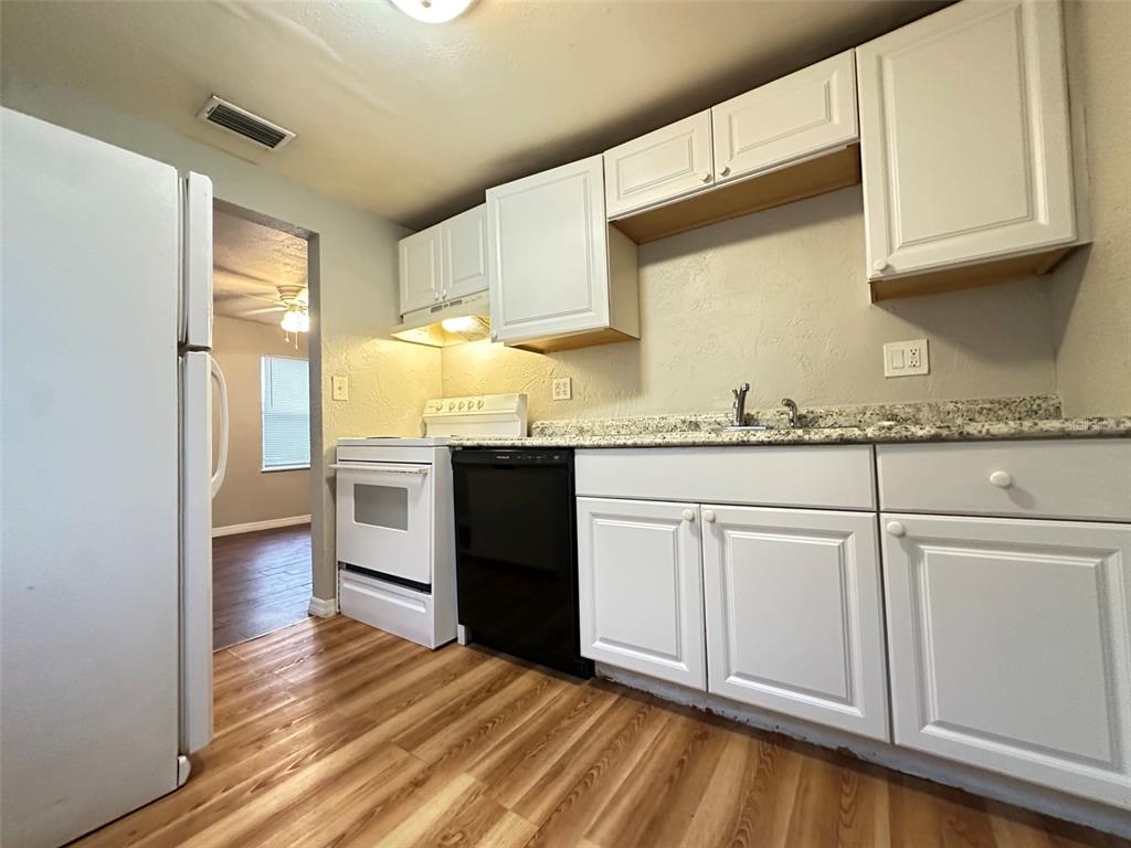 A kitchen features white cabinets, granite countertops, a black dishwasher, and wood-look flooring — 4111 28TH STREET N, ST PETERSBURG, FL