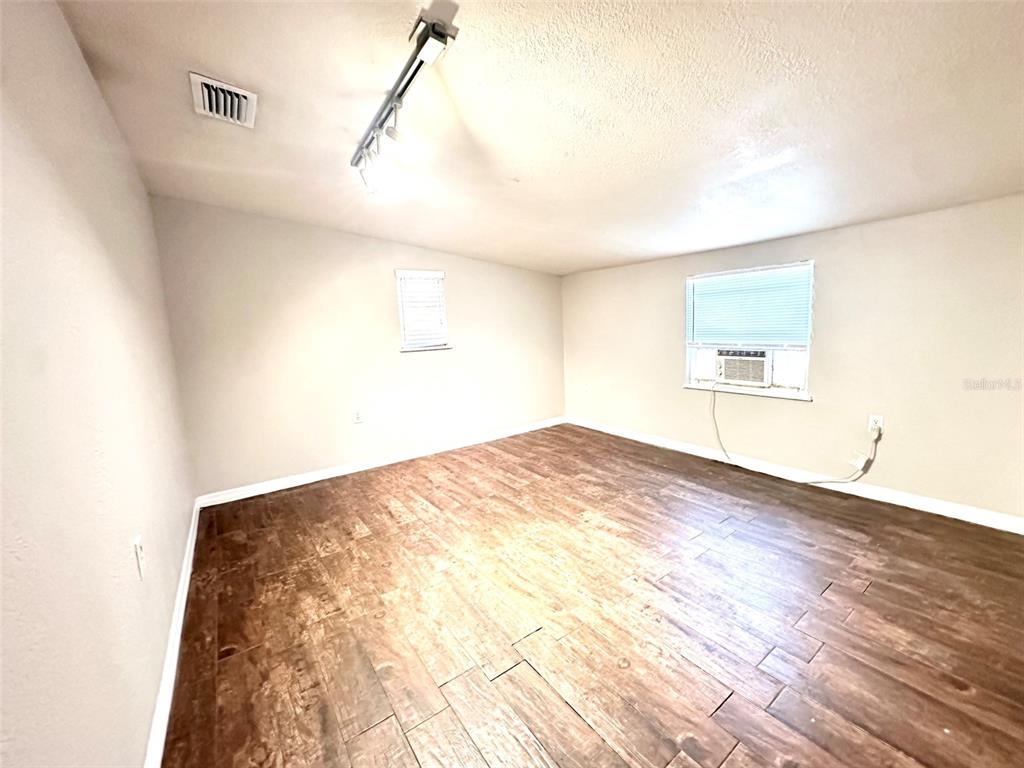 An empty room features wood-look tile flooring, white walls, a ceiling track light, and windows — 4111 28TH STREET N, ST PETERSBURG, FL