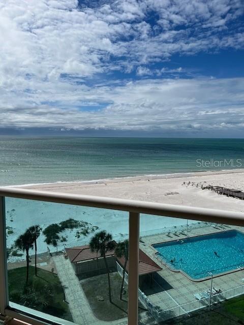 A balcony view overlooking a swimming pool, sandy beach, and the ocean under a cloudy sky — 880 MANDALAY AVENUE UNIT S713, CLEARWATER BEACH, FL