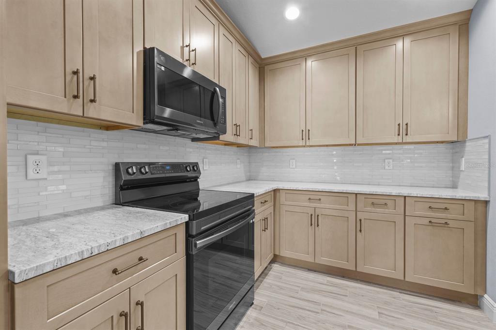 A kitchen with light wood cabinets, white countertops, a subway tile backsplash, and black appliances — 13218 BARNEVELDE RD, WEEKI WACHEE, FL