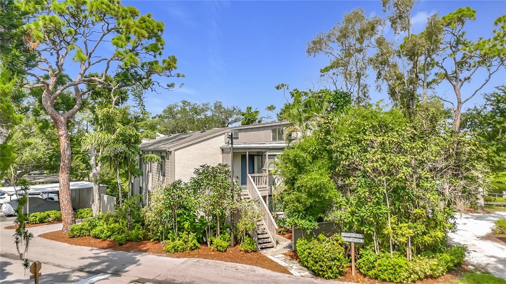 A two-story building with tan siding and a wooden staircase surrounded by lush trees — 1601 PELICAN POINT DRIVE UNIT 215, SARASOTA, FL
