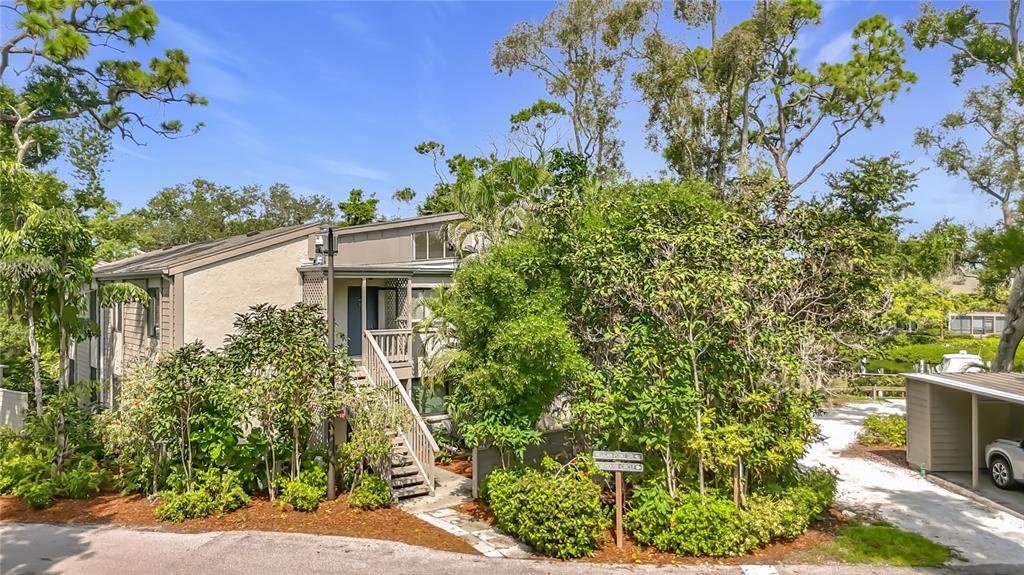 An exterior view of a multi-story residential building with wooden stairs and lush landscaping — 1601 PELICAN POINT DRIVE UNIT 215, SARASOTA, FL