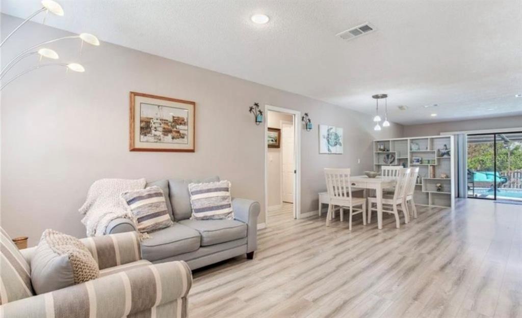 A living room and dining area with light wood-look flooring and neutral walls — 5875 BAY PINES LAKES BOULEVARD, ST PETERSBURG, FL