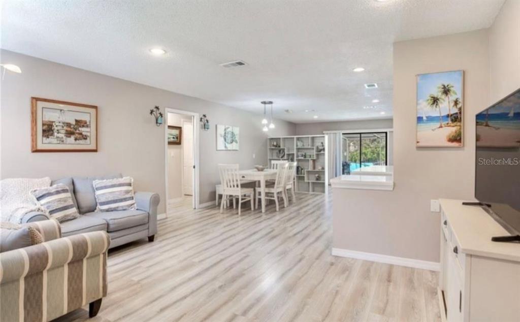 An open-concept living and dining area features light wood-look flooring and neutral wall paint — 5875 BAY PINES LAKES BOULEVARD, ST PETERSBURG, FL