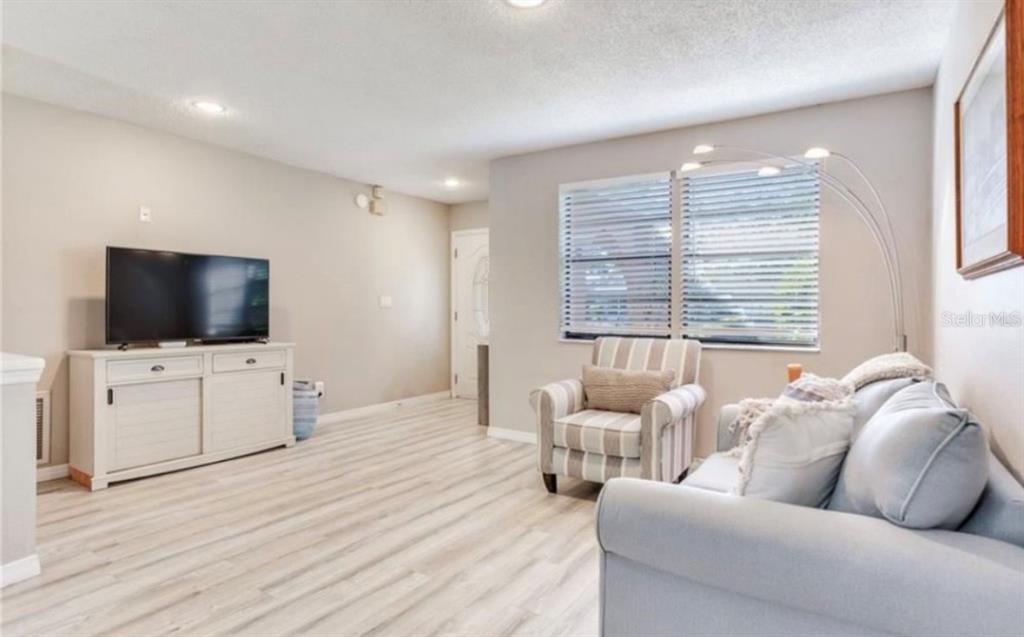 A living room features light wood-look flooring, a television on a white console, and seating — 5875 BAY PINES LAKES BOULEVARD, ST PETERSBURG, FL