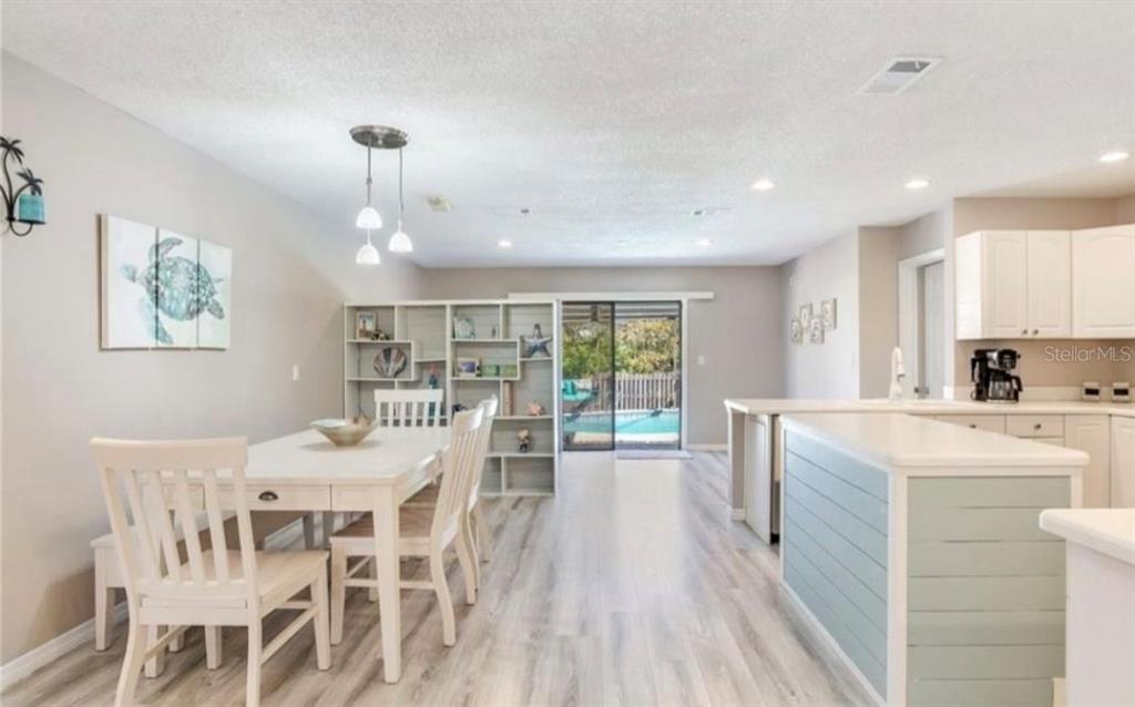 A dining area with white furniture and a bookshelf opens to a kitchen and pool view — 5875 BAY PINES LAKES BOULEVARD, ST PETERSBURG, FL