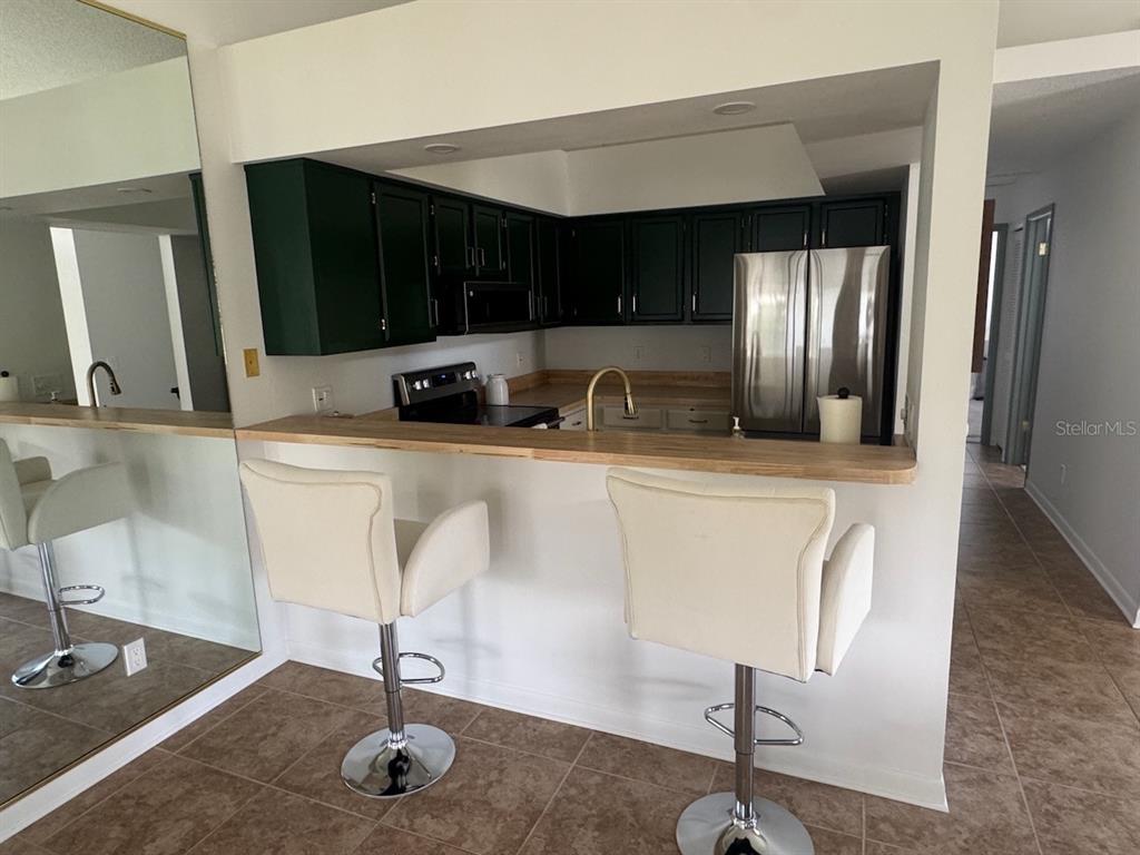 A kitchen features dark green cabinets, a light wood breakfast bar, and two white stools — 2749 COUNTRYSIDE BOULEVARD UNIT 20, CLEARWATER, FL
