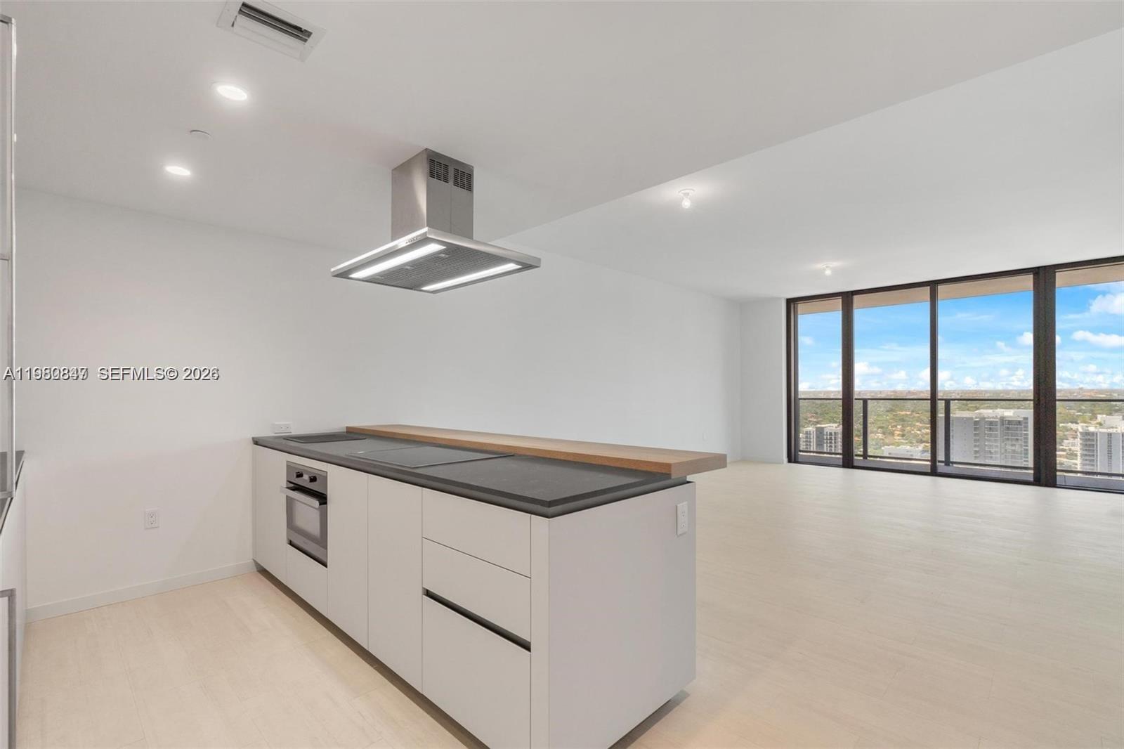 A modern kitchen island with a cooktop and hood sits in an open-plan room — 1000 Brickell Plz # 3310, Miami FL 33131, MIAMI, FL