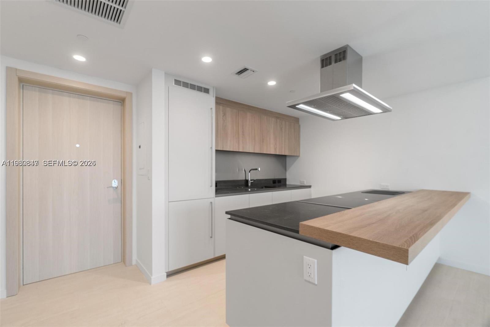 A modern kitchen features white cabinetry, wood-toned upper cabinets, a black countertop, and an island — 1000 Brickell Plz # 3310, Miami FL 33131, MIAMI, FL