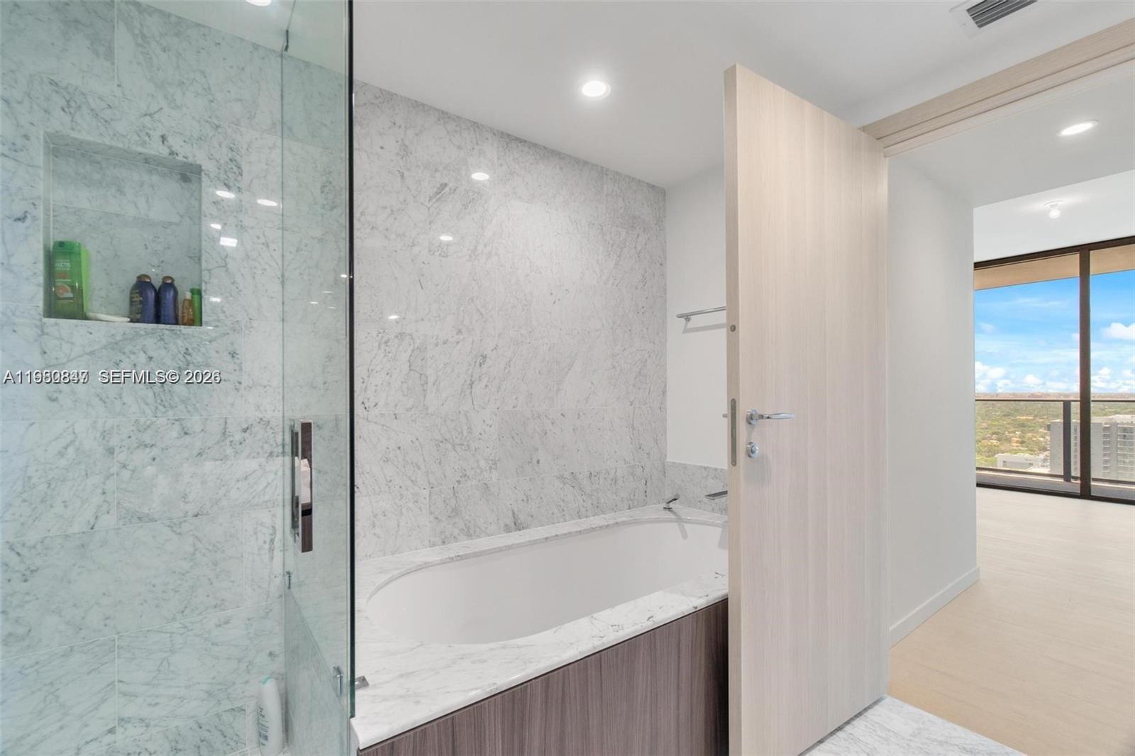 A bathroom features a marble-tiled shower and bathtub enclosure with a light wood door — 1000 Brickell Plz # 3310, Miami FL 33131, MIAMI, FL