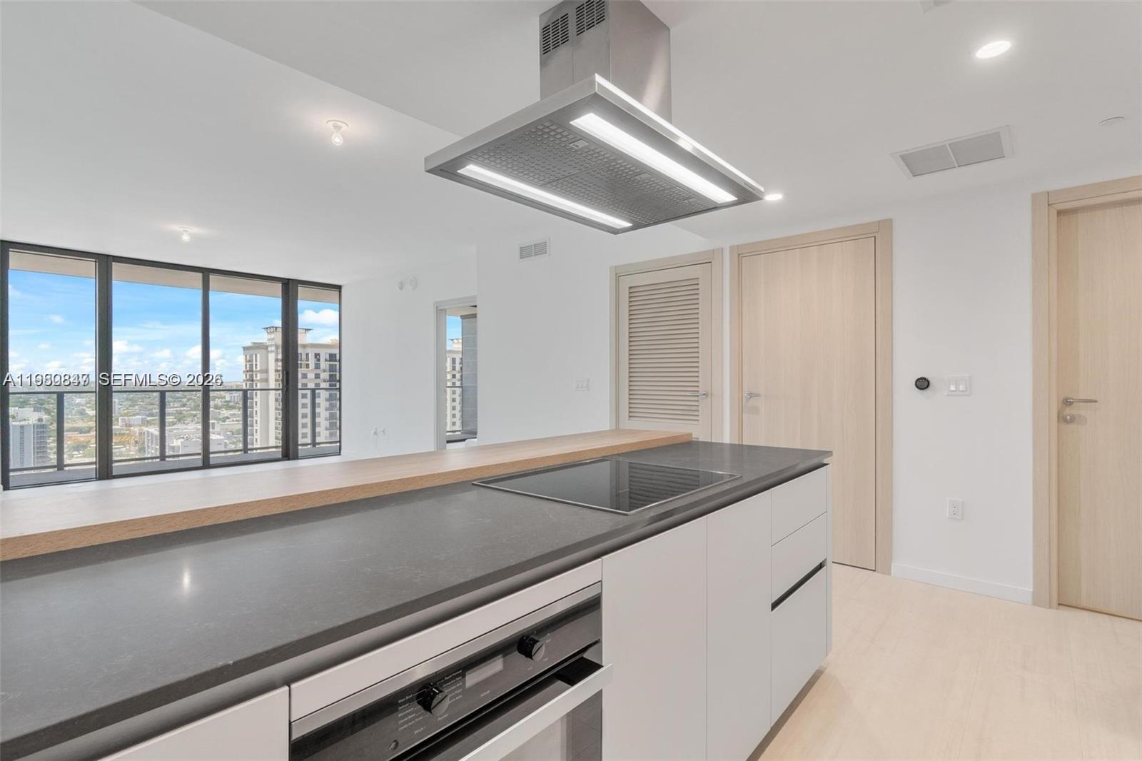 A modern kitchen features a central island with a cooktop, oven, and wood-topped breakfast bar — 1000 Brickell Plz # 3310, Miami FL 33131, MIAMI, FL