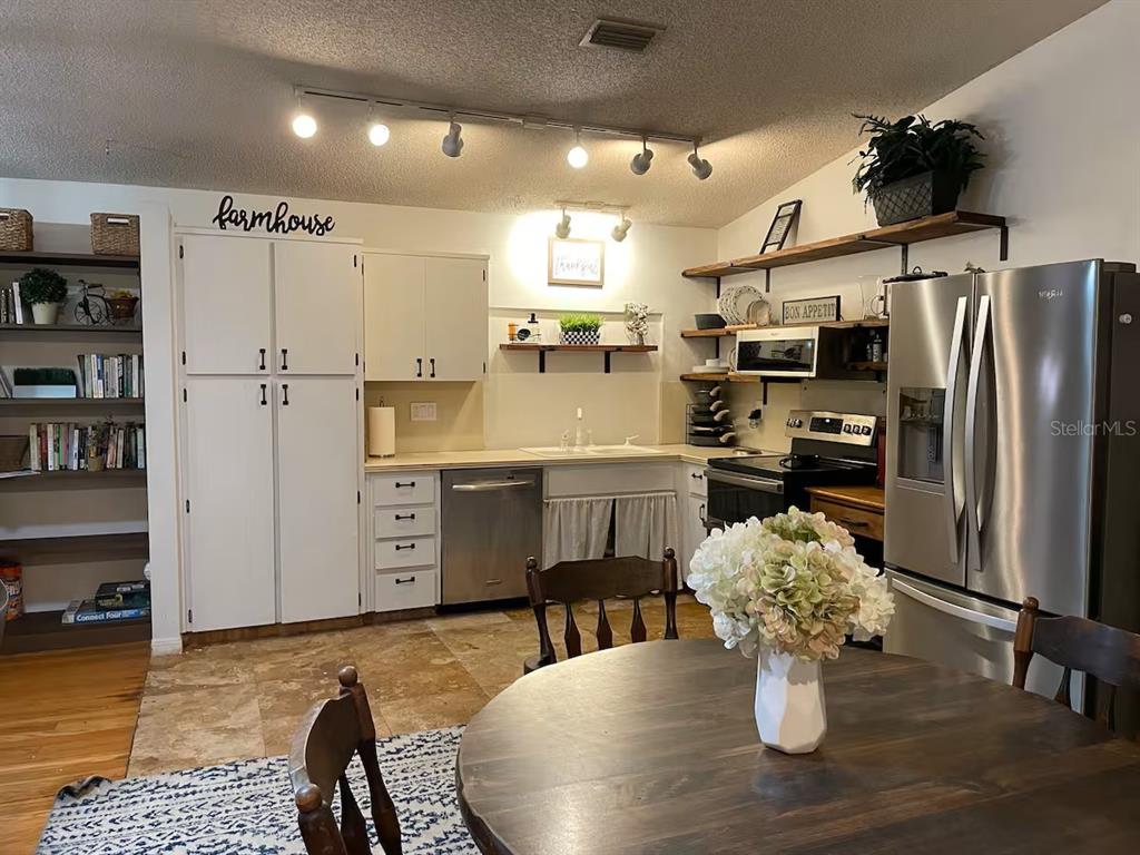 A kitchen features white cabinetry, open shelving, stainless steel appliances, and a round dining table — 2107 GROVE VALLEY AVENUE, PALM HARBOR, FL