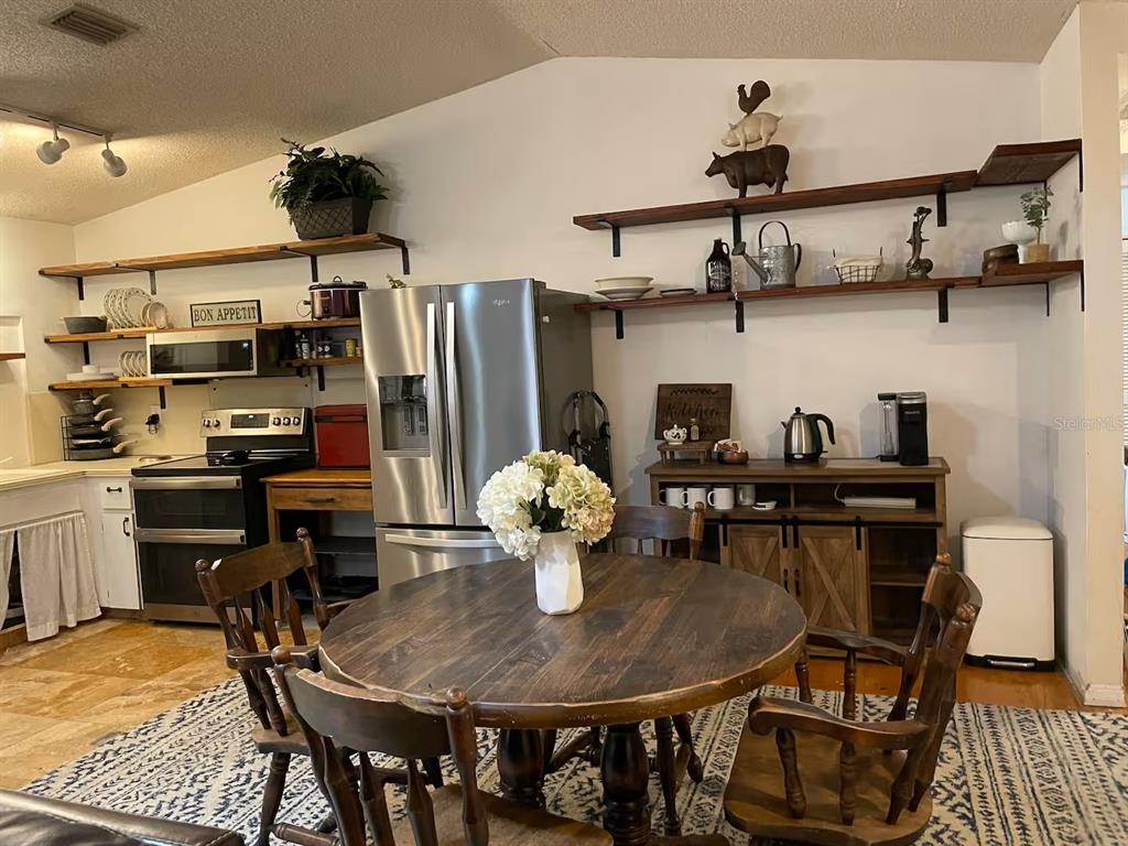 A kitchen features a round wooden dining table, open shelving, stainless steel appliances, and tile flooring — 2107 GROVE VALLEY AVENUE, PALM HARBOR, FL