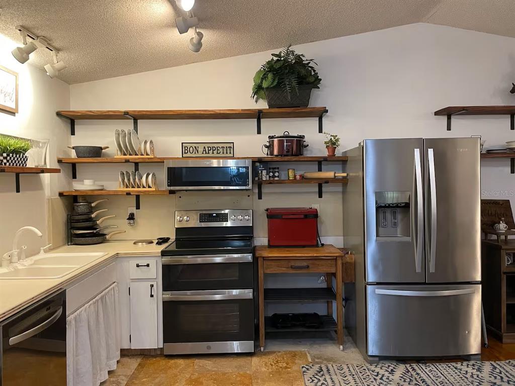 A kitchen features white cabinets, open wood shelving, stainless steel appliances, and tile flooring — 2107 GROVE VALLEY AVENUE, PALM HARBOR, FL
