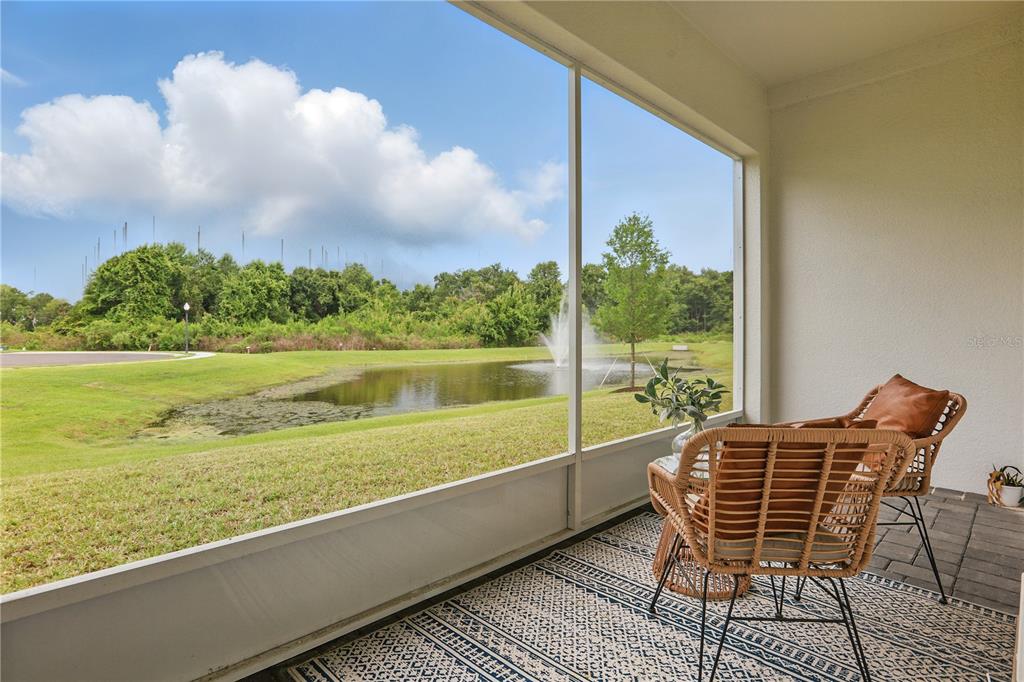 A screened-in patio overlooks a grassy lawn, a pond with a fountain, and trees — 1462 BROOKDALE COURT, OVIEDO, FL