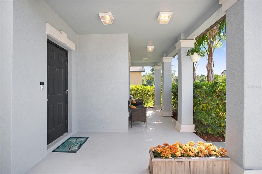 A covered front porch features a black door, light blue walls, and a wooden planter — 6342 COBBLE BLISS STREET, ZEPHYRHILLS, FL