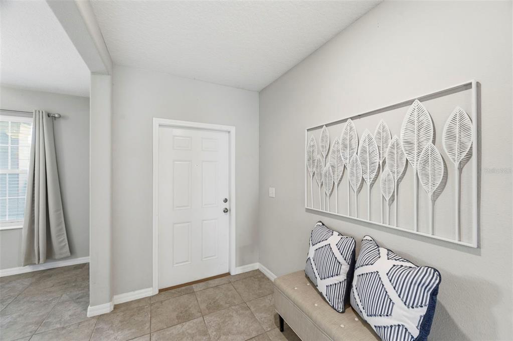 An entryway features a white front door, tiled flooring, a bench, and wall-mounted leaf art — 6342 COBBLE BLISS STREET, ZEPHYRHILLS, FL