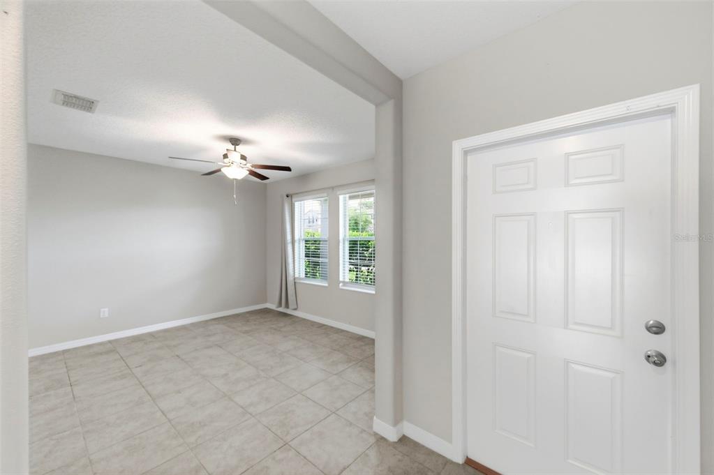 A room with light tile flooring, a ceiling fan, and a white front door — 6342 COBBLE BLISS STREET, ZEPHYRHILLS, FL