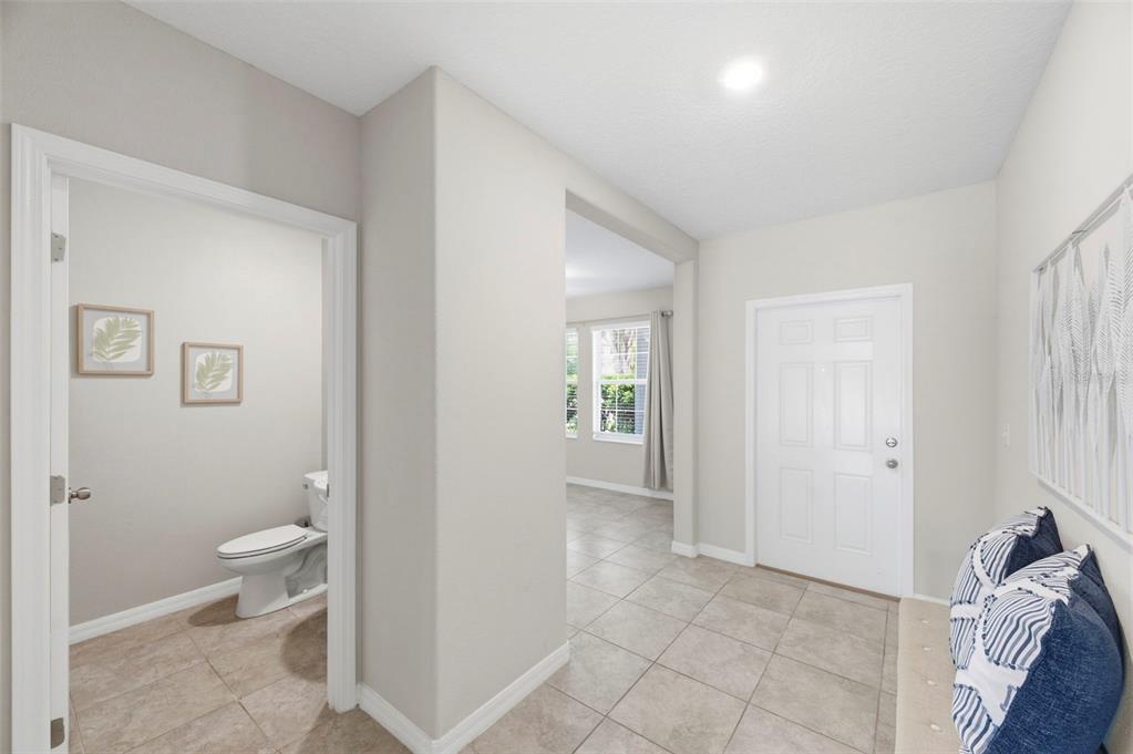 A tiled entryway features a half bathroom on the left and a front door ahead — 6342 COBBLE BLISS STREET, ZEPHYRHILLS, FL