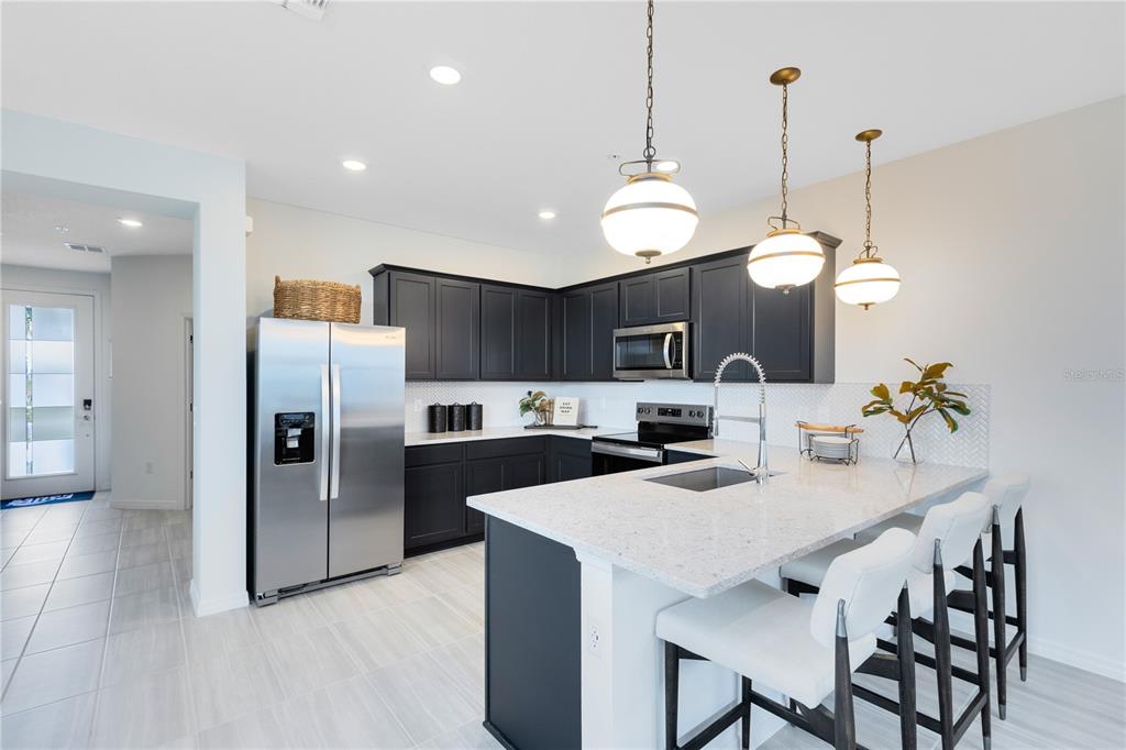 A modern kitchen features dark cabinets, stainless steel appliances, a quartz island, and pendant lighting — 6373 ARGENT WOOD DRIVE, WINTER GARDEN, FL