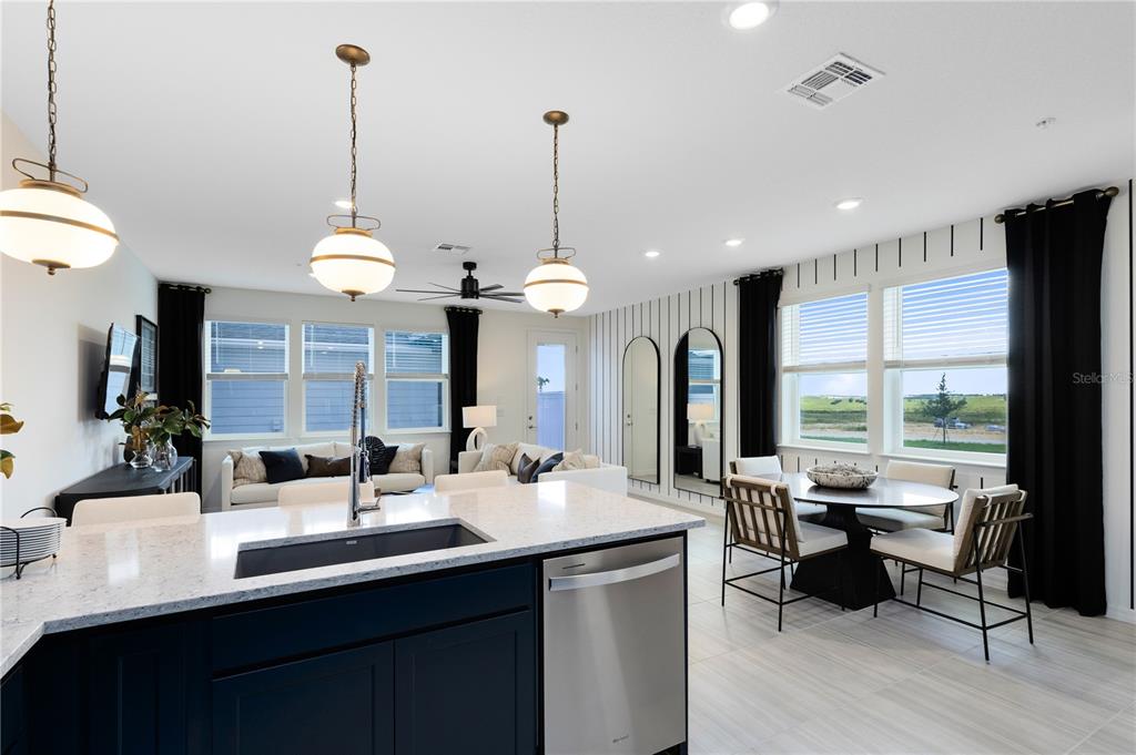 A kitchen island with a sink overlooks an open-concept living and dining area with windows — 6373 ARGENT WOOD DRIVE, WINTER GARDEN, FL