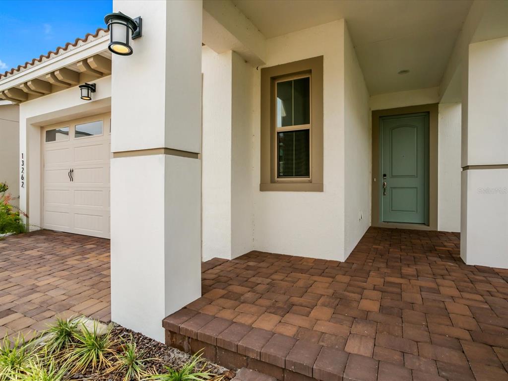 A paved walkway leads to a covered entryway with a light blue door and garage — 13262 WINTERTON LANE, ORLANDO, FL