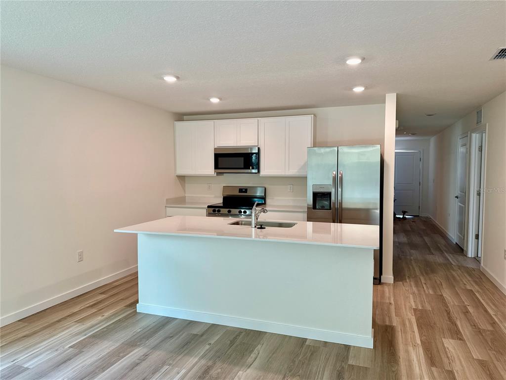 A kitchen features white cabinets, stainless steel appliances, a center island, and wood-look flooring — 7773 SW 46TH COURT, OCALA, FL
