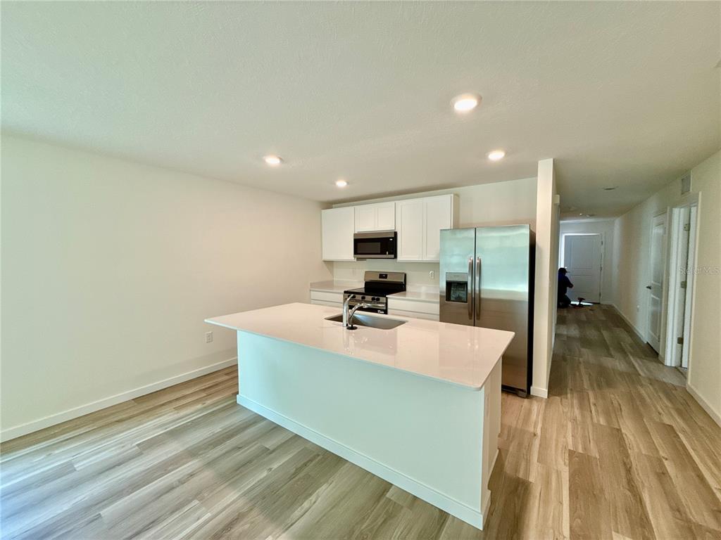 A modern kitchen features a white island, stainless steel appliances, and light wood-look flooring — 7773 SW 46TH COURT, OCALA, FL