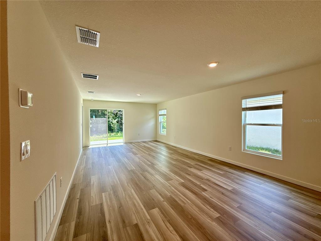 An empty living room features light wood-look flooring, white walls, recessed lighting, and sliding doors — 7773 SW 46TH COURT, OCALA, FL