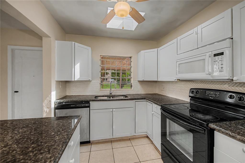 A kitchen features white cabinets, dark granite countertops, a black stove, and a window — 21450 OLEAN BOULEVARD, PORT CHARLOTTE, FL